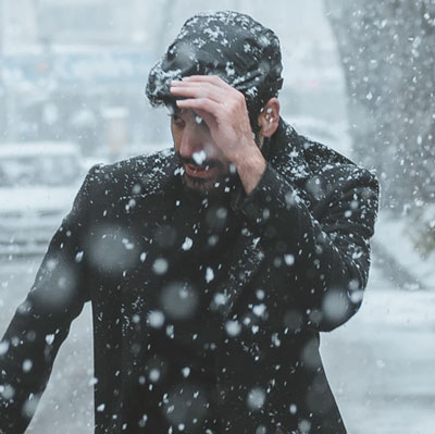 Man pulling newsboy cap down over eyes in snow
