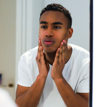 Young Black man washing face in mirror