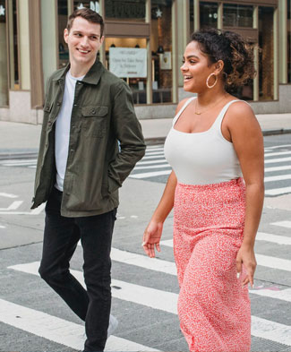 A man and woman smile while walking down the street together 