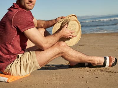 Man sitting on beach wearing slides