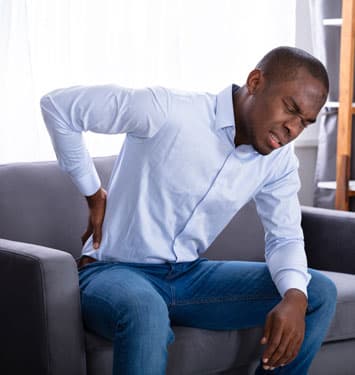 A man with back pain sitting on a living room chair
