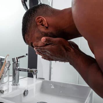 Bearded man washing face at sink