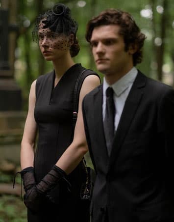 A man with a black suit next to a woman with a black dress at a funeral 