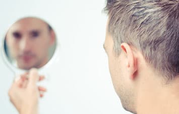 Man looking at himself in handheld mirror