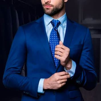 Man in blue suit doing up shirt cuff buttons