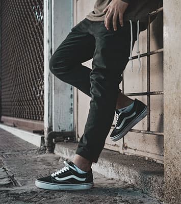 Guy leaning against a wall wearing Vans Old Skool sneakers