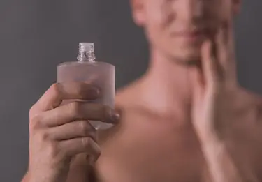 Man holding up aftershave while rubbing his face