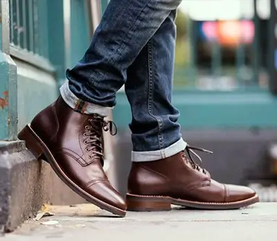 Close up of man wearing dark brown cap toe boots with blue jeans