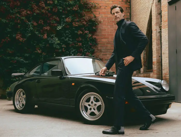 Man wearing turtleneck and jacket in front of Porsche