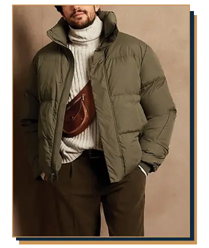 Man wearing an olive green puffer jacket from Banana Republic layered over an off-white ribbed turtleneck sweater with dark trousers and a brown leather crossbody bag.
