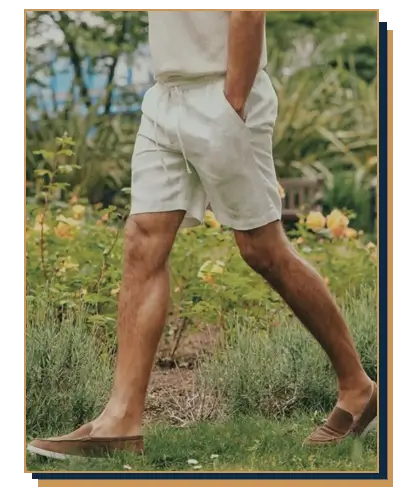 Man walking in a garden wearing off-white linen drawstring shorts and brown suede loafers