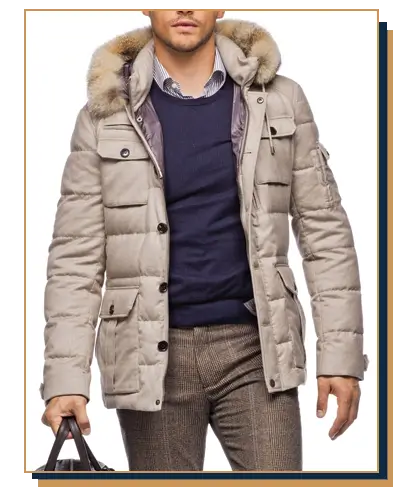 Man wearing a beige hooded parka coat with fur trim from Suit Supply, layered over a navy crewneck sweater, striped dress shirt, and tailored patterned trousers.