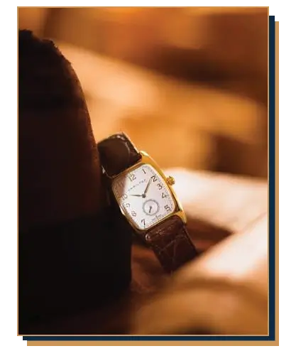 Hamilton Boulton vintage-style gold dress watch with a white dial, sub-seconds dial, and brown leather strap resting against a fedora hat
